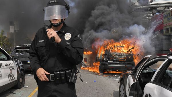 Полицейский Лос-Анджелеса на фоне горящей машины во время протестов  - Sputnik Южная Осетия