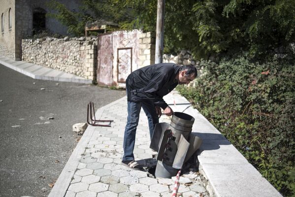 Местный житель у не разорвавшегося снаряда на улице города Мартуни. Город Мартуни в Карабахе подвергся обстрелу - Sputnik Южная Осетия