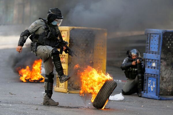 Офицер израильской полиции пинает горящую покрышку во время антиизраильской акции протеста в Хевроне на Западном берегу - Sputnik Южная Осетия