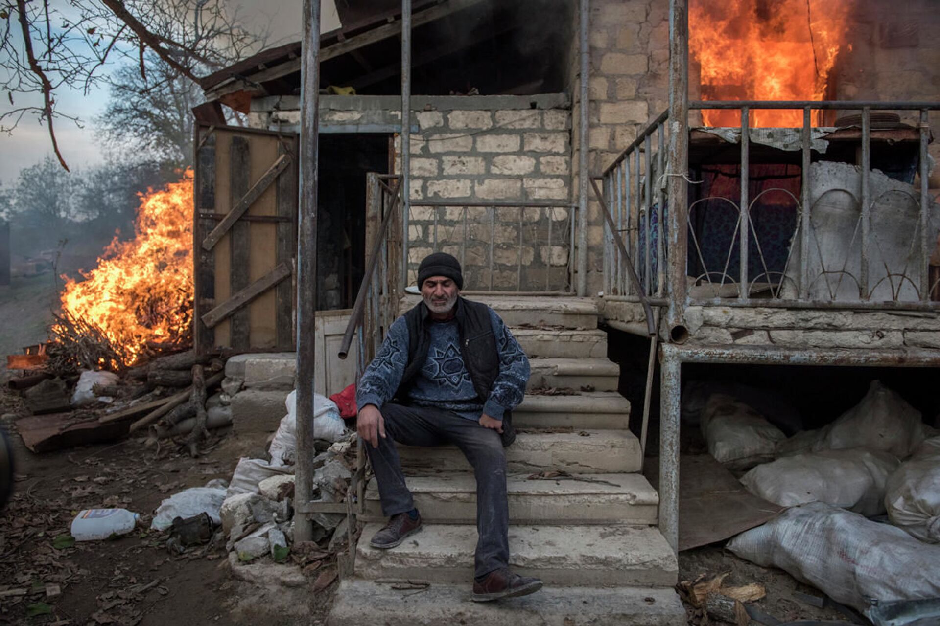 Местный житель Арег сидит у горящего дома в поселке Карегах, Нагорный Карабах. Некоторые жители сожгли свои дома перед тем как уйти - Sputnik Южная Осетия, 1920, 03.05.2022