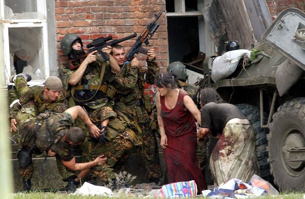 Российский спецназовец (слева) несет раненого коллегу, пока двое солдат и две женщины укрываются за БТР во время спасательной операции в школе Беслана. Северная Осетия, 3 сентября 2004 года. - Sputnik Южная Осетия
