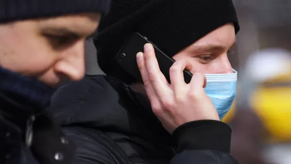 Молодой человек в медицинской маске разговаривает по телефону - Sputnik Южная Осетия