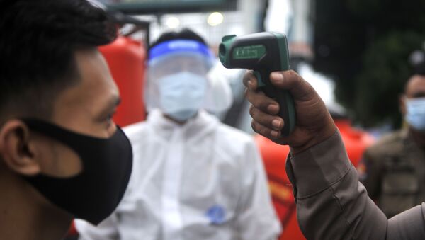  Сотрудник полиции измеряет температуру тела у верующего у мечети Аль-Машун в провинции Северная Суматра в Индонезии. - Sputnik Южная Осетия