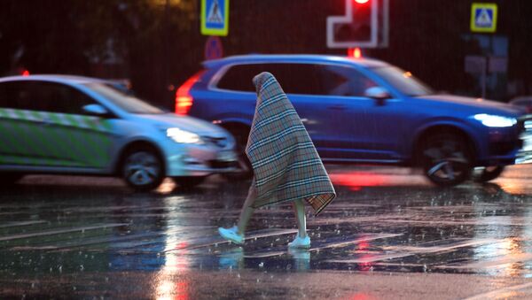 Прохожий переходит дорогу во время дождя в Москве, накрывшись пледом - Sputnik Южная Осетия