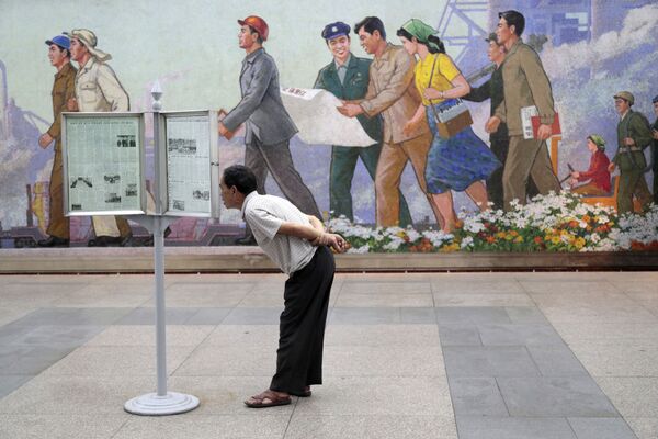 Пассажир метро в Пхеньяне читает газету на стенде - Sputnik Южная Осетия